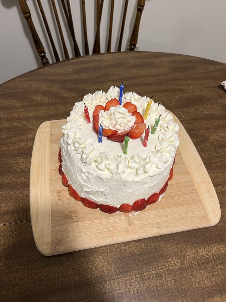 A homemade whipped cream cake decorated with strawberries and colorful candles.
